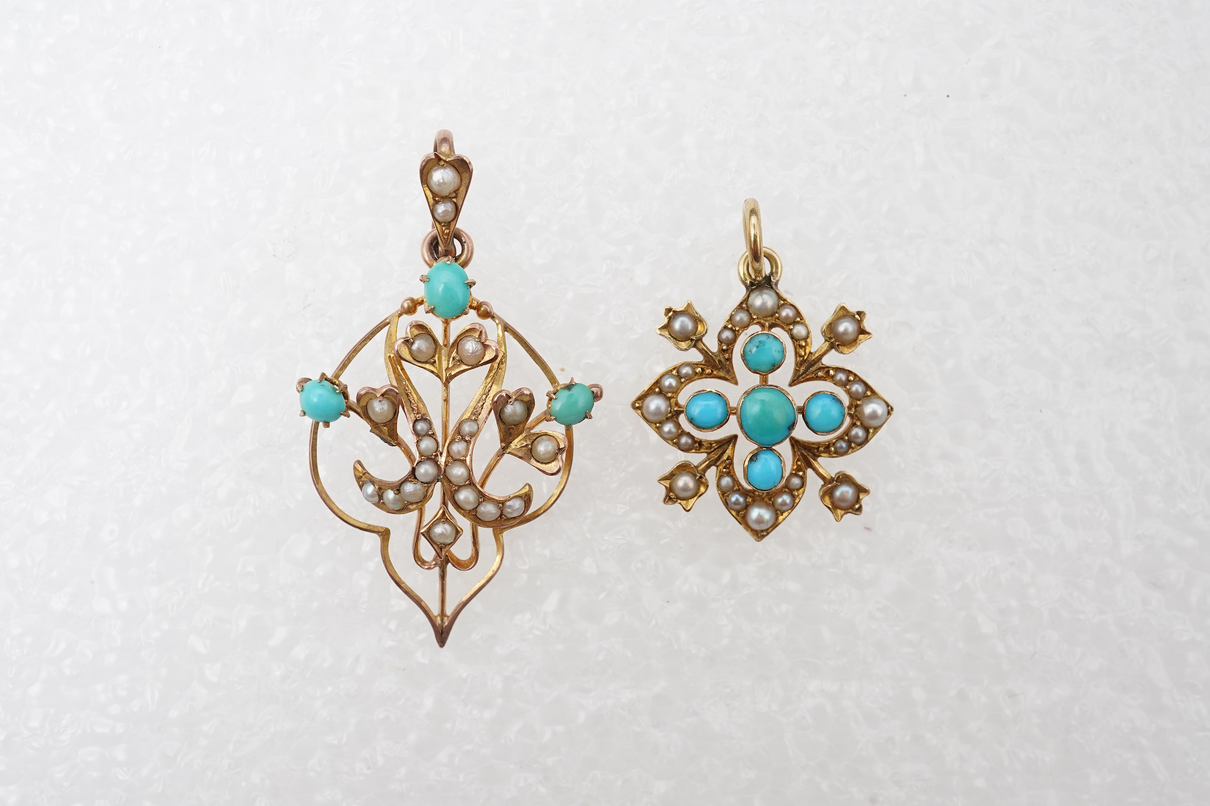 Two Edwardian turquoise and seed pearl pendants, each of foliate design, set with turquoise cabochons and seed pearls, mounted in gold, longest 3.7cm, smaller stamped 15CT, combined gross weight approximately 4 grams
